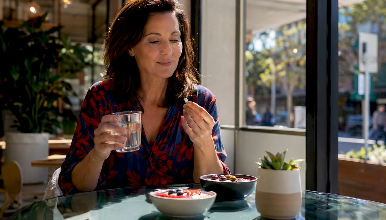 Woman taking beauty supplement at kitchen table