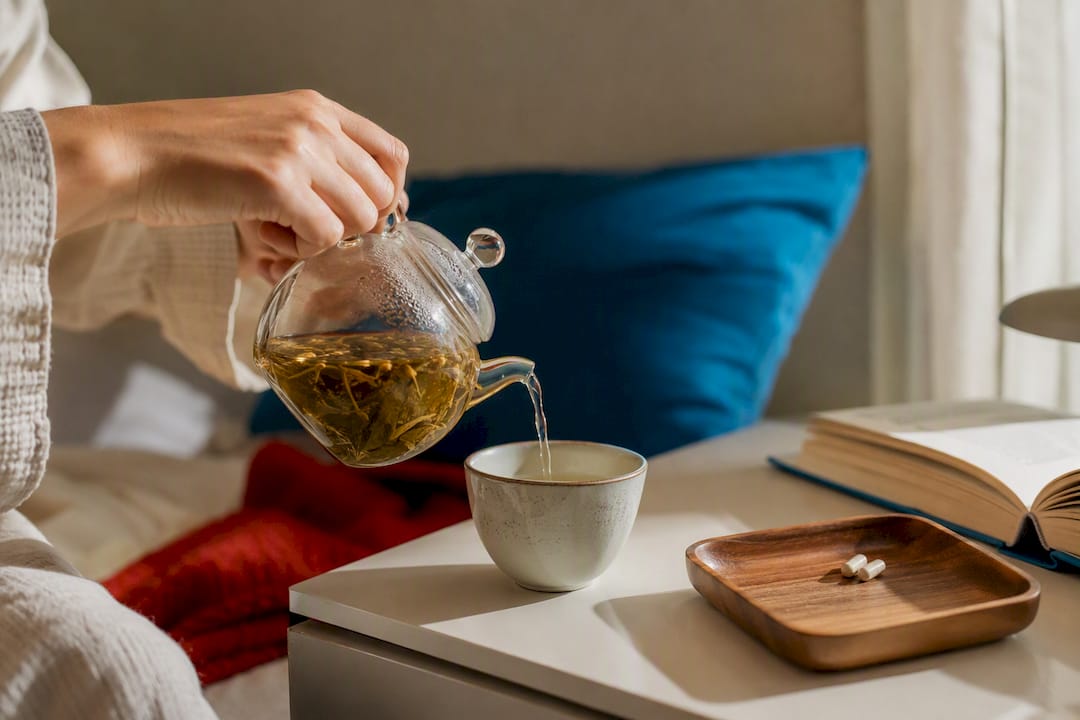Hand holding melatonin supplement near capsules and water glass